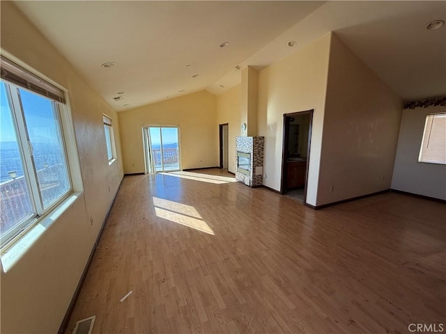 unfurnished living room with light wood-type flooring, vaulted ceiling, and a stone fireplace