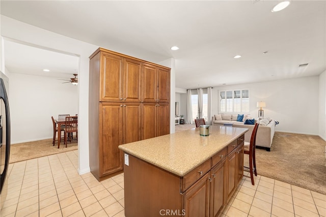 kitchen with refrigerator with ice dispenser, ceiling fan, a kitchen island, and light carpet