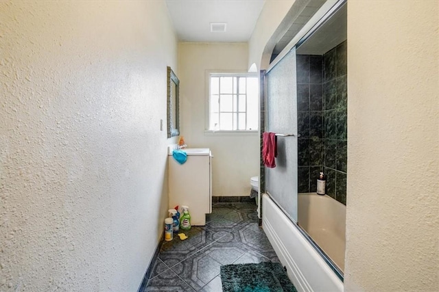 bathroom featuring toilet and bath / shower combo with glass door