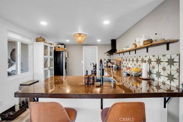 kitchen featuring hardwood / wood-style floors, wall chimney range hood, sink, decorative backsplash, and stainless steel fridge with ice dispenser