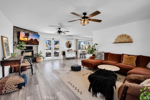 living room featuring french doors, ceiling fan, a fireplace, wood-type flooring, and a wall unit AC