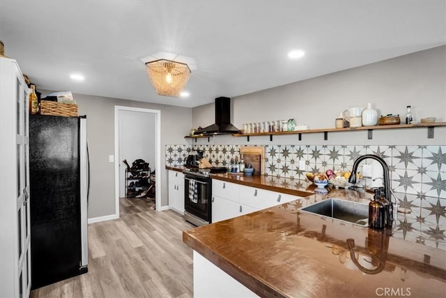 kitchen with black refrigerator, sink, wall chimney range hood, light hardwood / wood-style floors, and stainless steel electric range oven