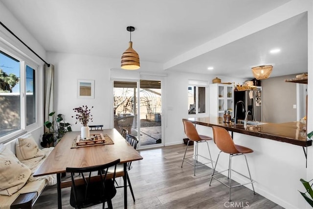 kitchen featuring pendant lighting, stainless steel refrigerator with ice dispenser, light wood-type flooring, kitchen peninsula, and a breakfast bar area