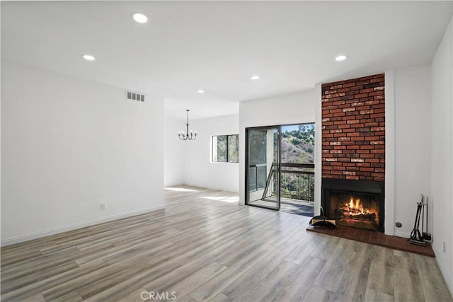 unfurnished living room with light hardwood / wood-style floors, a brick fireplace, and a notable chandelier