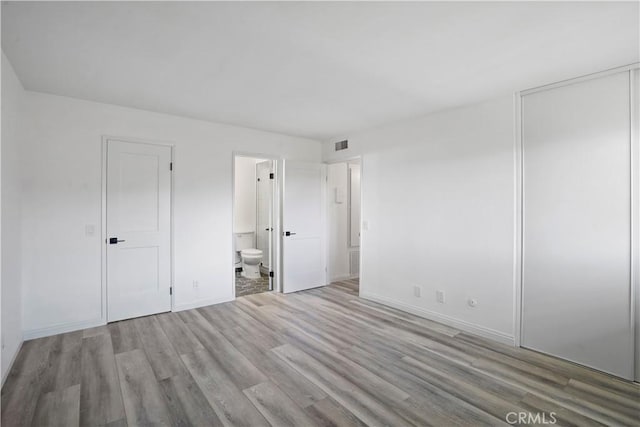 unfurnished bedroom with light hardwood / wood-style flooring and ensuite bath