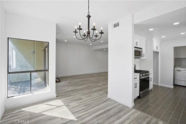 kitchen with an inviting chandelier, white cabinets, stainless steel appliances, and washer / dryer