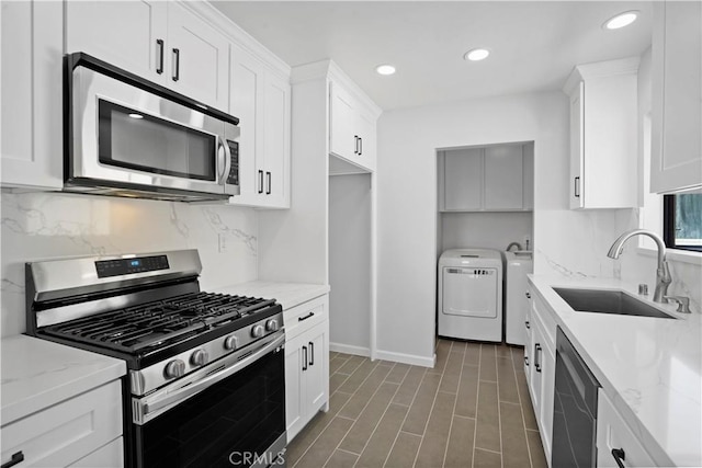 kitchen with white cabinets, sink, light stone countertops, independent washer and dryer, and stainless steel appliances