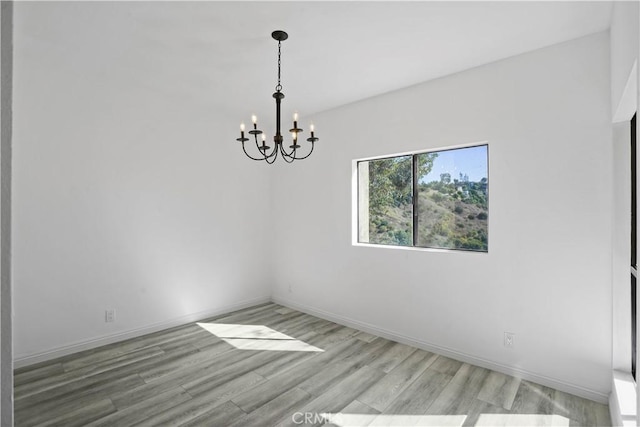 spare room with light wood-type flooring and a notable chandelier