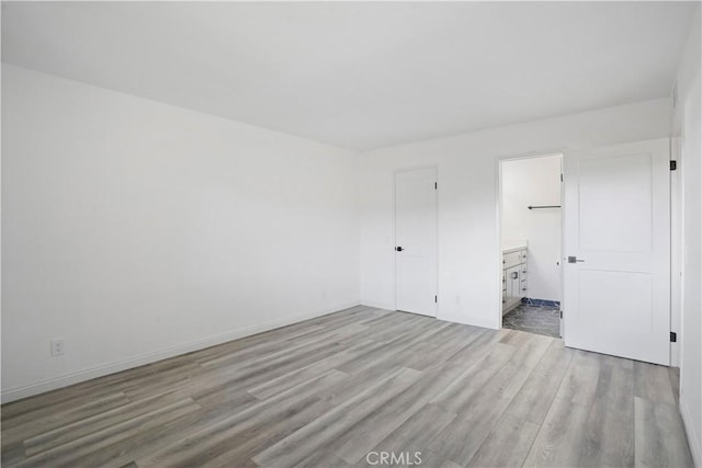 unfurnished bedroom featuring ensuite bathroom and light hardwood / wood-style flooring