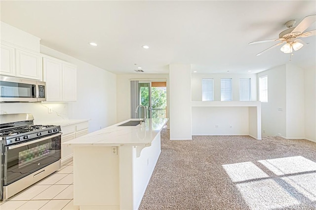 kitchen featuring stainless steel appliances, sink, white cabinetry, a kitchen bar, and an island with sink