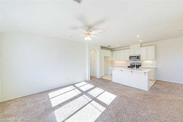 kitchen with a center island with sink, light colored carpet, ceiling fan, a kitchen bar, and white cabinetry