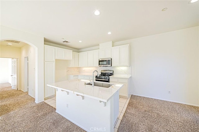 kitchen featuring a center island with sink, white cabinetry, appliances with stainless steel finishes, light carpet, and sink