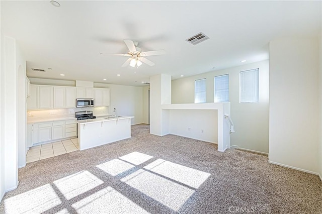 kitchen with a center island with sink, light colored carpet, white cabinetry, appliances with stainless steel finishes, and sink