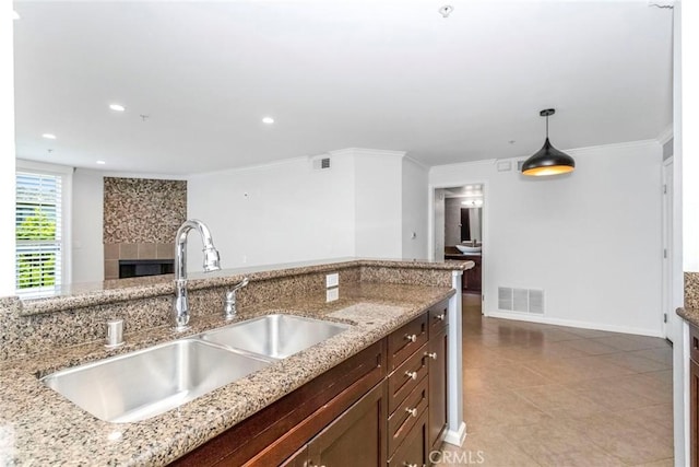 kitchen with decorative light fixtures, light stone counters, sink, and crown molding