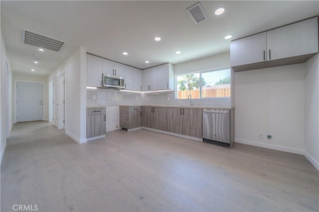 kitchen featuring sink, white cabinets, light hardwood / wood-style floors, decorative backsplash, and appliances with stainless steel finishes