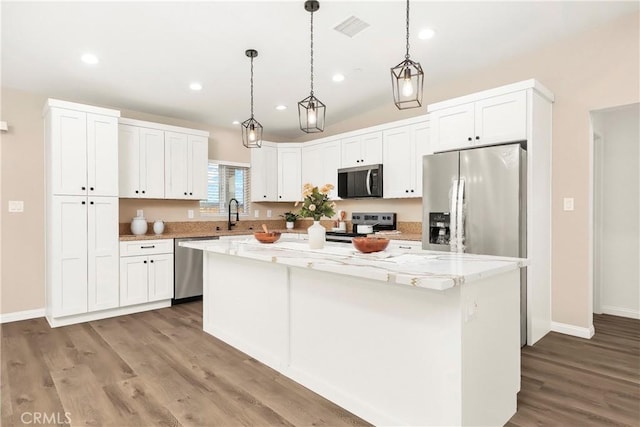 kitchen with a center island, visible vents, hanging light fixtures, appliances with stainless steel finishes, and white cabinets