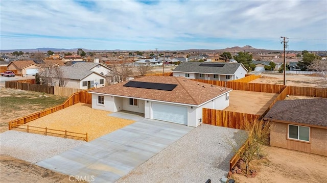 view of front of home featuring an attached garage, roof mounted solar panels, a residential view, a fenced backyard, and driveway