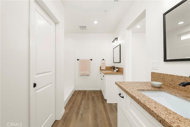 full bathroom featuring recessed lighting, two vanities, a sink, and wood finished floors