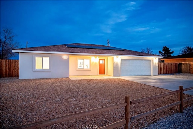 ranch-style house with stucco siding, an attached garage, roof mounted solar panels, fence, and driveway