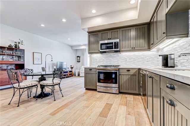 kitchen with sink, stainless steel appliances, gray cabinets, decorative backsplash, and light wood-type flooring