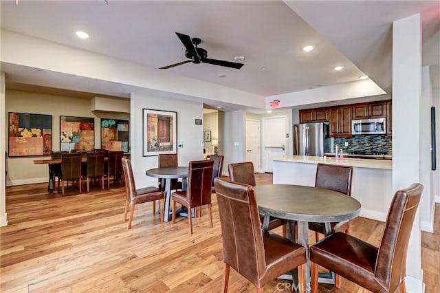 dining area with light hardwood / wood-style floors, ceiling fan, and a tray ceiling