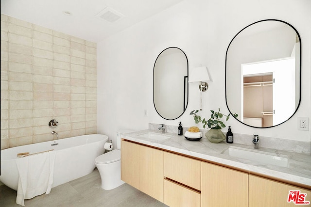 bathroom with a washtub, vanity, and toilet