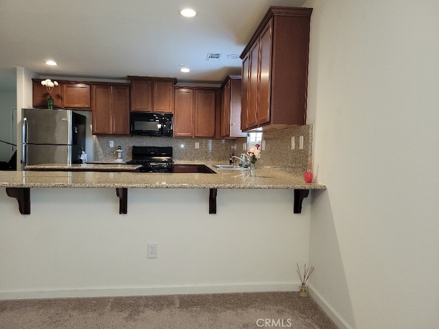 kitchen featuring kitchen peninsula, a kitchen breakfast bar, light stone countertops, sink, and black appliances