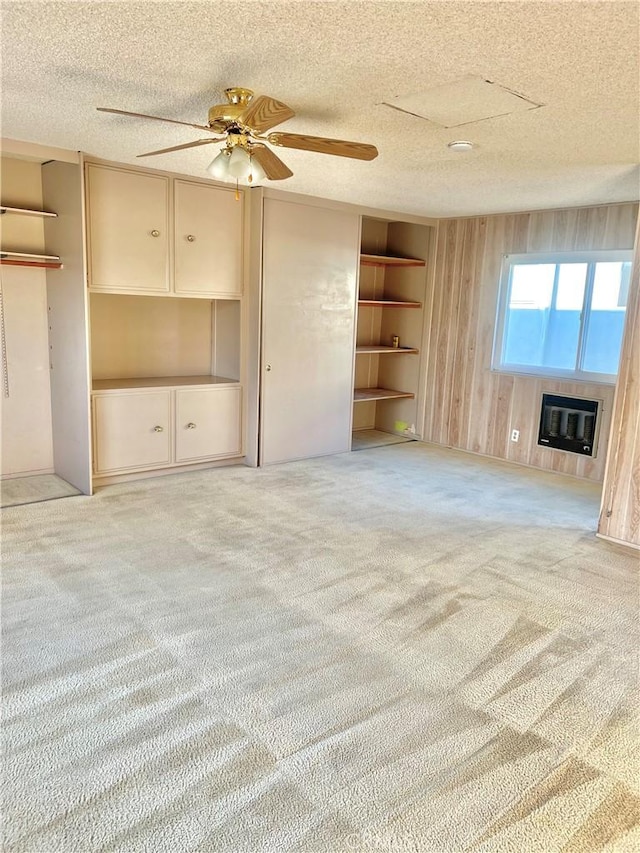 unfurnished living room with heating unit, built in features, wooden walls, light carpet, and a textured ceiling