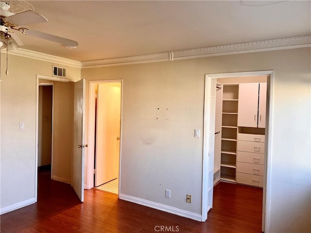 unfurnished bedroom with dark wood-type flooring, a walk in closet, ornamental molding, and a closet