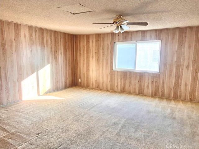 carpeted spare room with ceiling fan, a textured ceiling, and wood walls