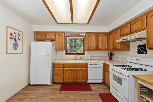 kitchen with tile counters, sink, white appliances, and light hardwood / wood-style flooring