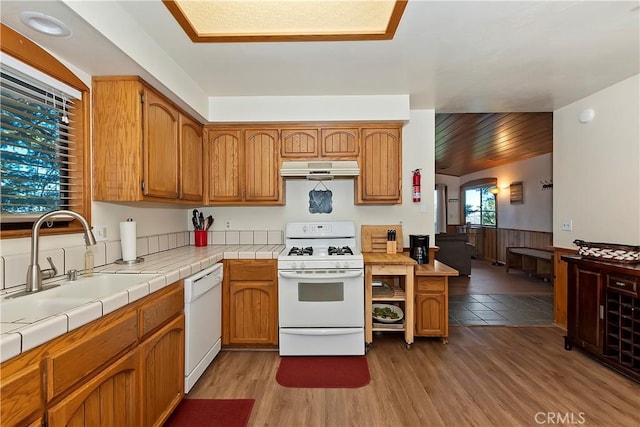 kitchen with white appliances, tile counters, wooden walls, light hardwood / wood-style floors, and sink