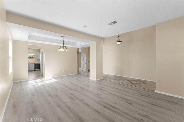 unfurnished living room featuring light hardwood / wood-style floors, a raised ceiling, and an inviting chandelier