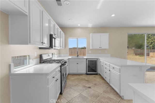 kitchen with kitchen peninsula, wine cooler, light tile patterned floors, appliances with stainless steel finishes, and white cabinetry