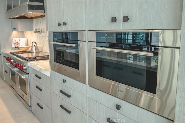 kitchen with mail area, appliances with stainless steel finishes, wall chimney exhaust hood, light countertops, and decorative backsplash