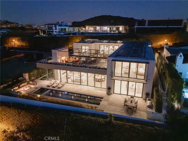 back house at twilight featuring a balcony and a patio area