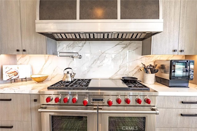 kitchen featuring range hood, range with two ovens, light stone countertops, and backsplash