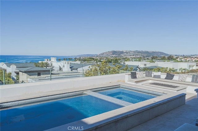 view of swimming pool with a fire pit, a water view, and an in ground hot tub