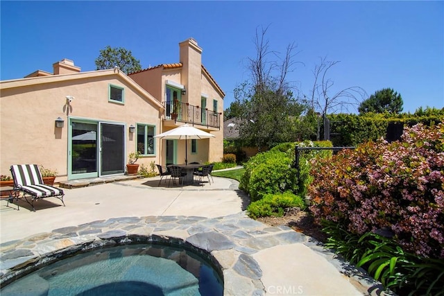 rear view of property featuring a patio area, a balcony, and an in ground hot tub