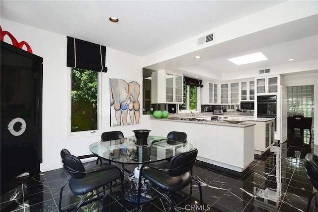 kitchen with kitchen peninsula, tasteful backsplash, black double oven, white cabinetry, and plenty of natural light