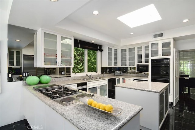 kitchen with light stone countertops, a skylight, white cabinetry, and double oven