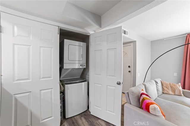 laundry room with dark wood-type flooring and stacked washer / drying machine