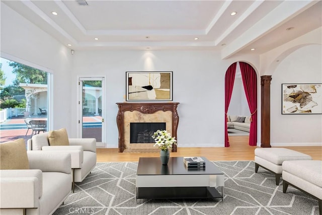 living room with decorative columns, a raised ceiling, a fireplace, and wood-type flooring