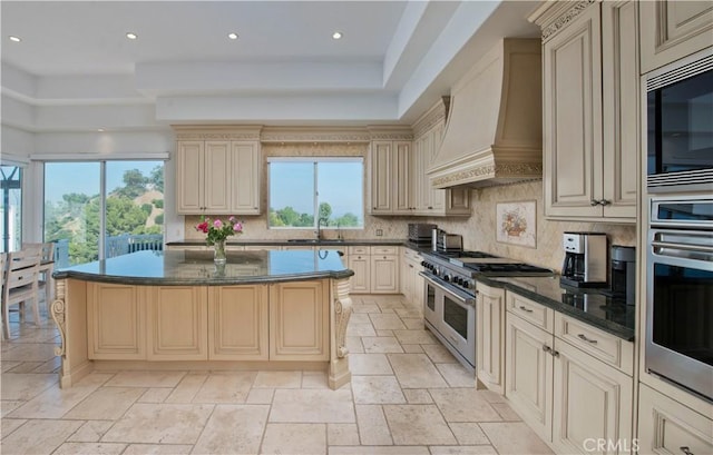 kitchen with a center island, tasteful backsplash, premium range hood, cream cabinets, and appliances with stainless steel finishes