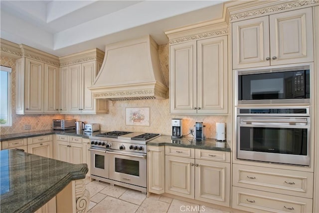 kitchen featuring cream cabinetry, custom range hood, backsplash, and appliances with stainless steel finishes