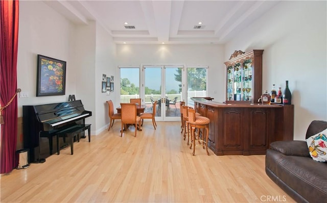 bar featuring beam ceiling, coffered ceiling, a high ceiling, and light wood-type flooring