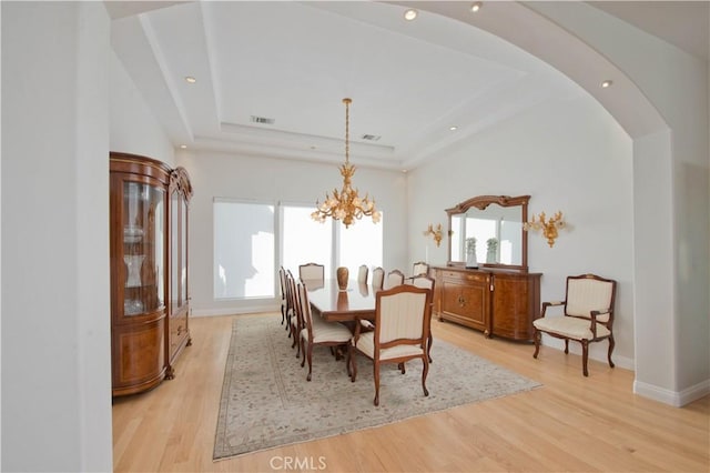 dining room featuring a raised ceiling, light hardwood / wood-style flooring, and a chandelier