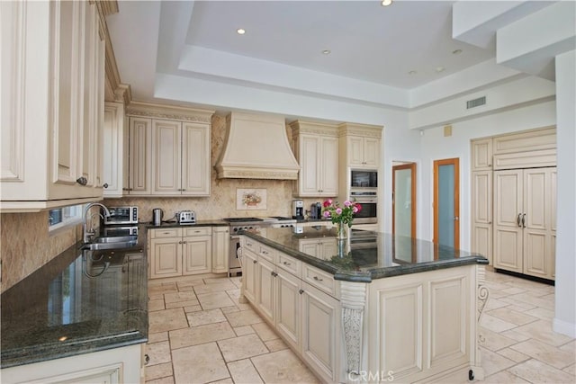 kitchen featuring appliances with stainless steel finishes, custom exhaust hood, sink, cream cabinets, and an island with sink