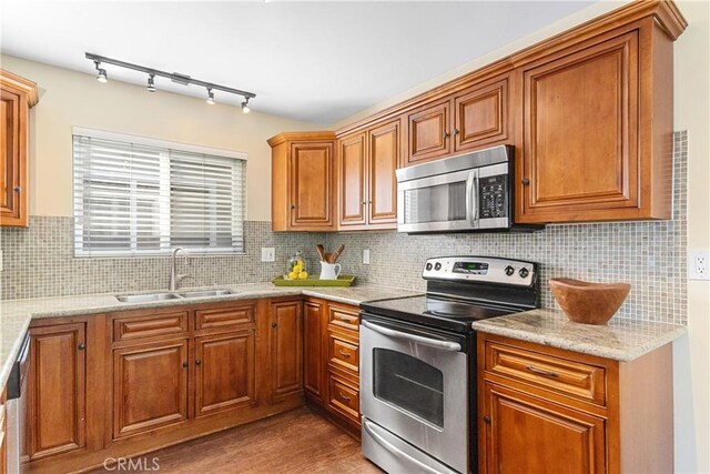 kitchen with wood-type flooring, sink, decorative backsplash, light stone counters, and stainless steel appliances