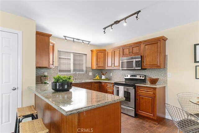 kitchen featuring dark wood-type flooring, a breakfast bar, stainless steel appliances, light stone counters, and kitchen peninsula